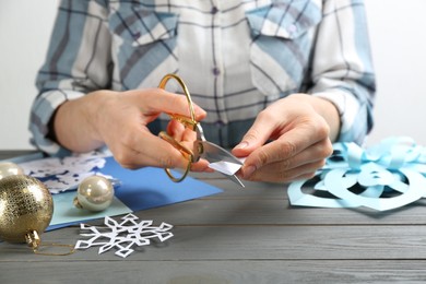 Woman making paper snowflake at grey wooden table, closeup