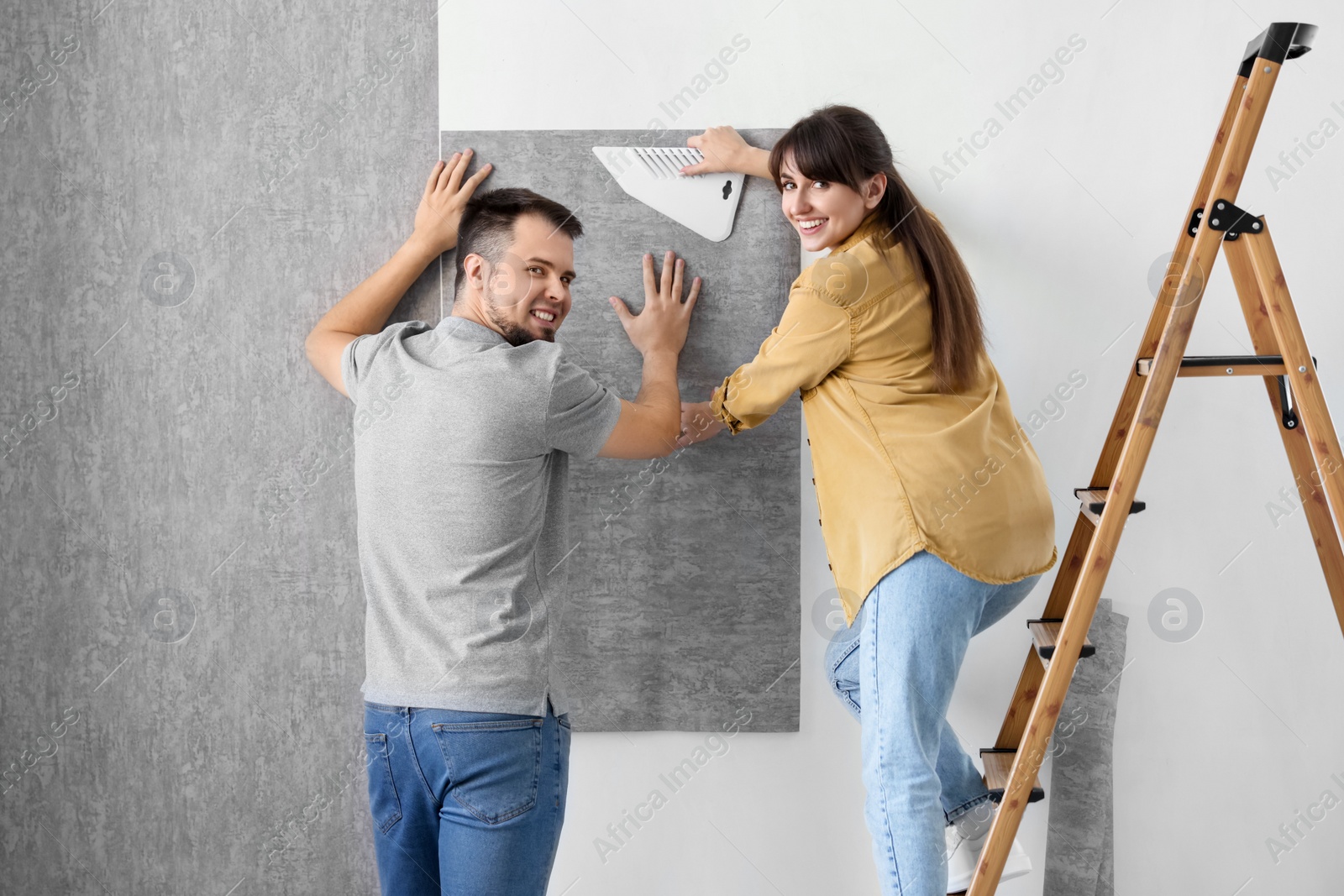 Photo of Couple hanging stylish gray wallpaper in room