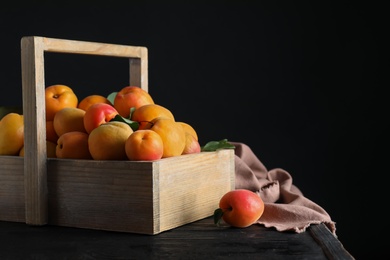 Many fresh ripe apricots in wooden basket on table against black background. Space for text