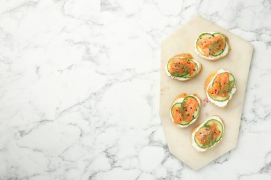 Photo of Tasty canapes with salmon, cucumber and cream cheese on white marble table, top view. Space for text