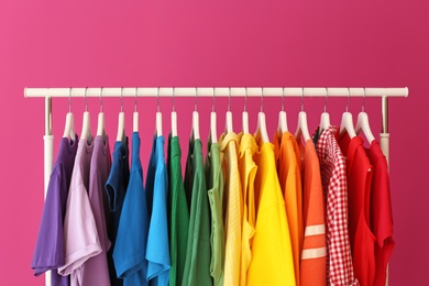 Rack with rainbow clothes on color background