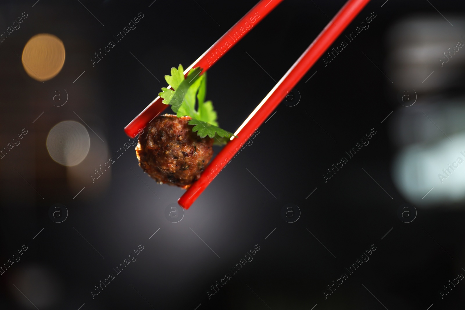 Photo of Chopsticks with meat ball on dark background, closeup. Space for text