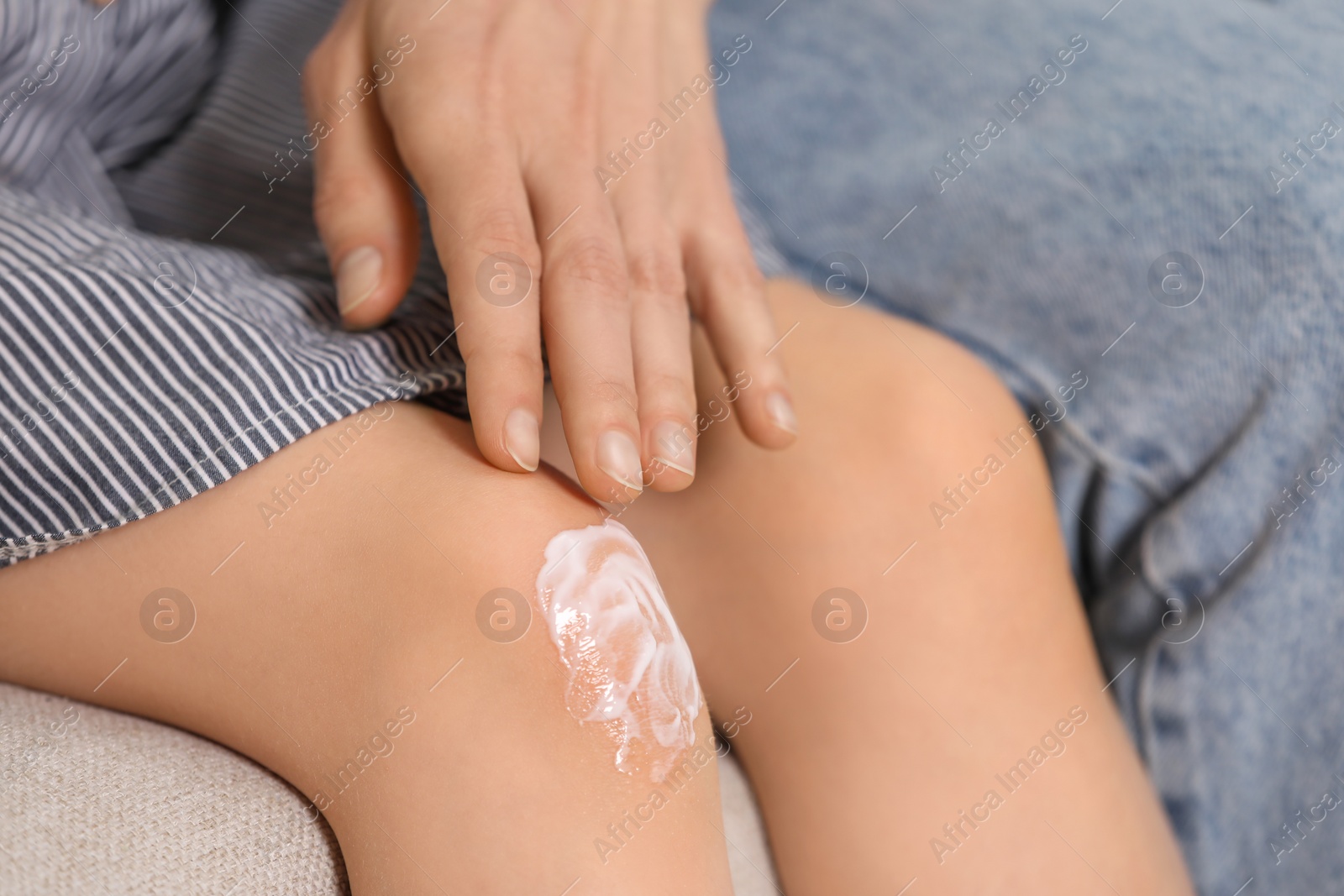 Photo of Mother applying ointment onto her daughter's knee on couch, closeup