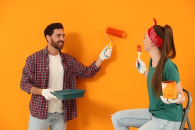 Man painting orange wall and happy woman holding can of dye with brush. Interior design