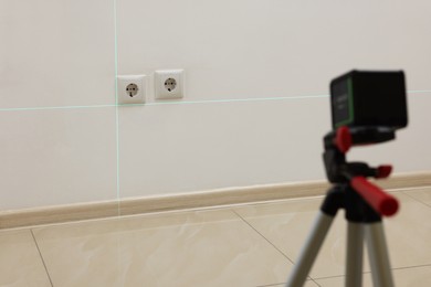 Photo of Using cross line laser level for accurate installation of outlet in white wall indoors