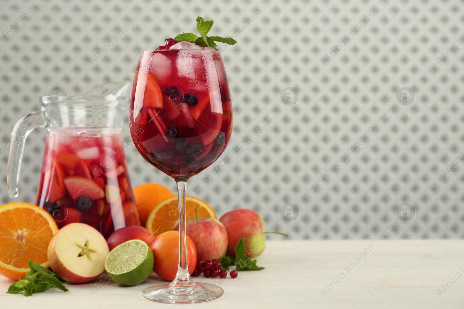 Photo of Glass and jug of Red Sangria with fruits on white wooden table, space for text