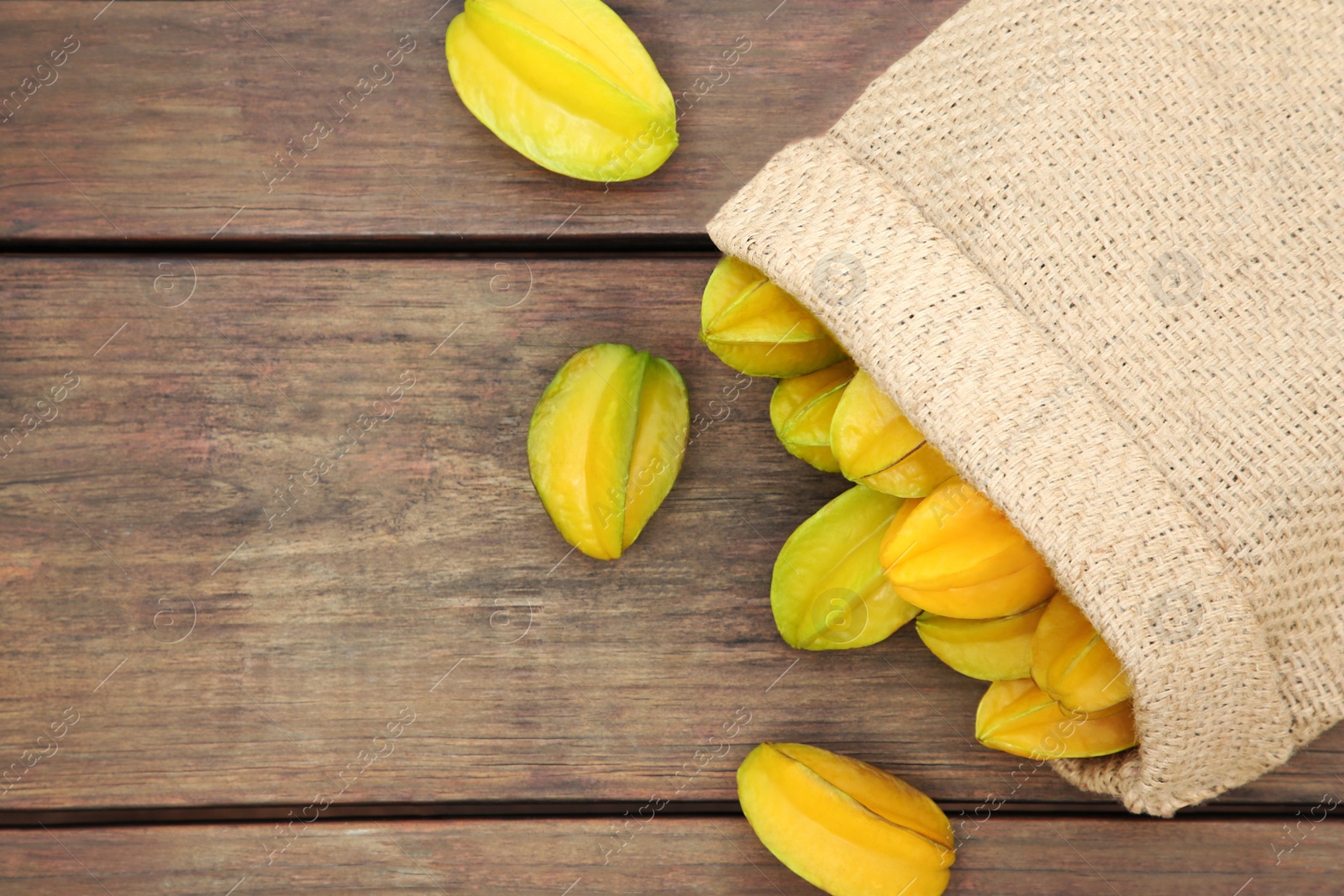 Photo of Sack with delicious ripe carambolas on wooden table, flat lay. Space for text