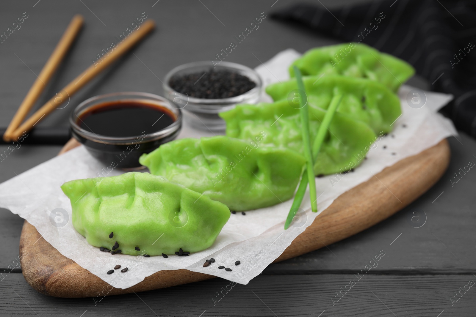 Photo of Delicious green dumplings (gyozas), soy sauce and sesame seeds on grey wooden table, closeup