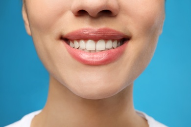 Woman with healthy teeth and beautiful smile on blue background, closeup. Cosmetic dentistry