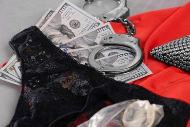 Prostitution concept. Women`s panties, condom, handcuffs and dollar banknotes on grey background, closeup