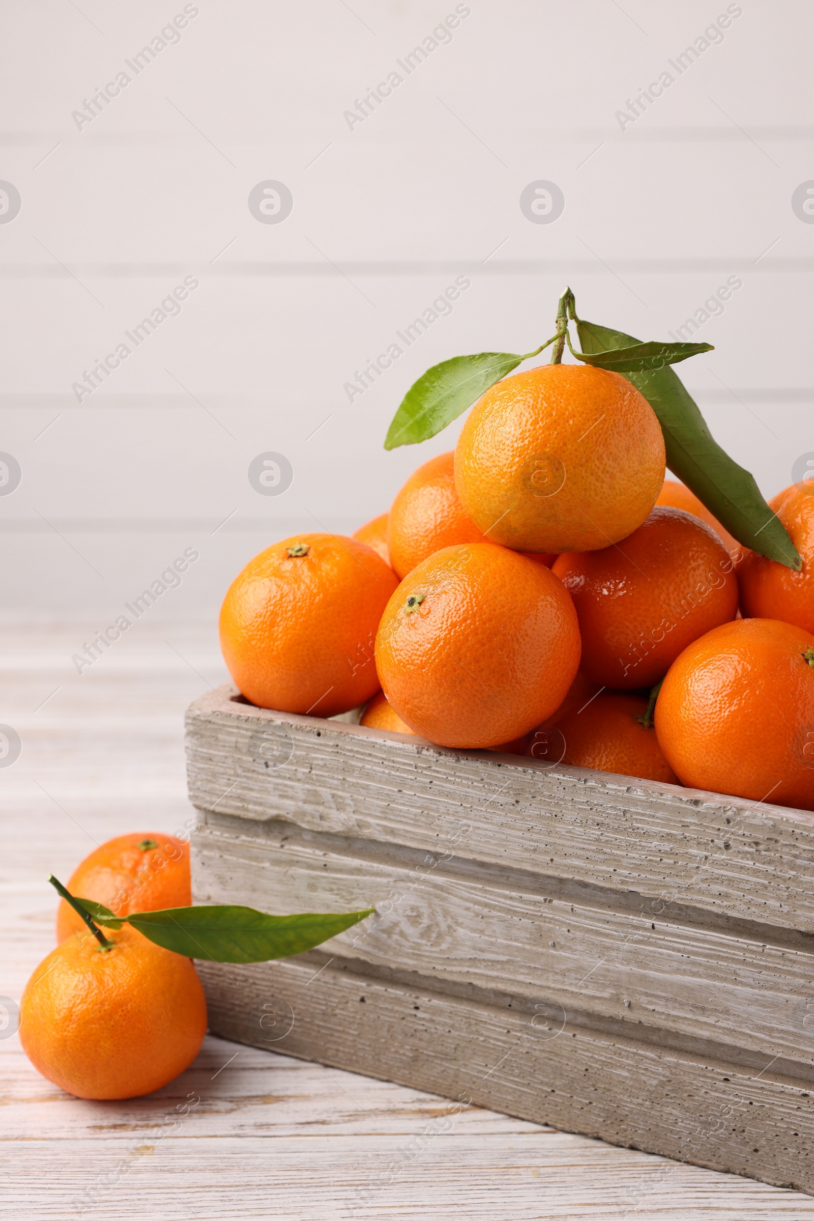 Photo of Delicious tangerines with leaves on light wooden table. Space for text