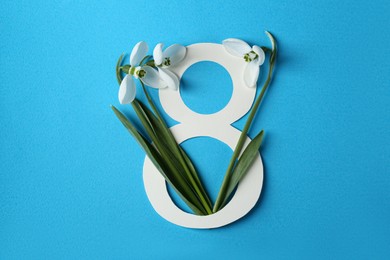 Beautiful snowdrops and paper number 8 on light blue background, flat lay