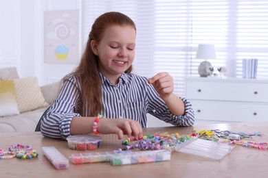 Photo of Cute girl making beaded jewelry at table indoors