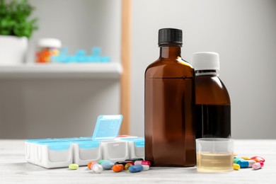 Photo of Bottles of syrup, measuring cup, weekly pill organizer and pills on table. Cold medicine