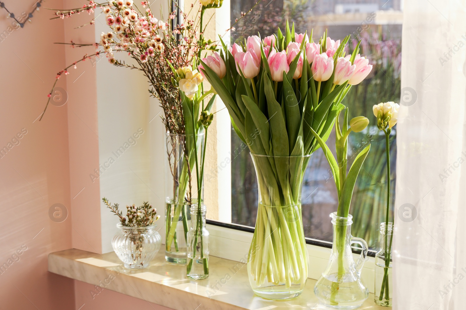 Photo of Many different spring flowers and branches with leaves on windowsill indoors