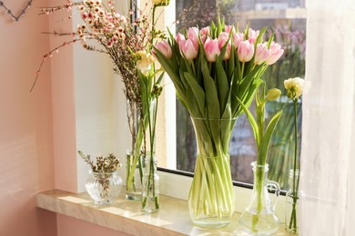 Photo of Many different spring flowers and branches with leaves on windowsill indoors