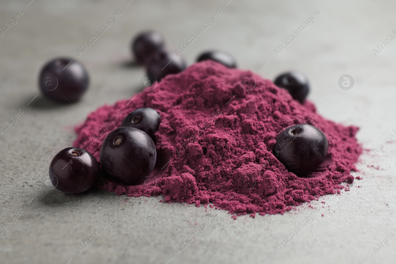 Photo of Heap of acai powder and berries on grey table, closeup