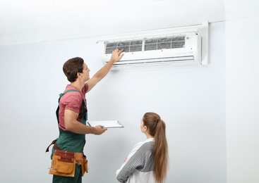 Male technician speaking with woman about air conditioner indoors