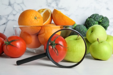 Photo of Fresh fruits, vegetables and magnifying glass on white table. Poison detection
