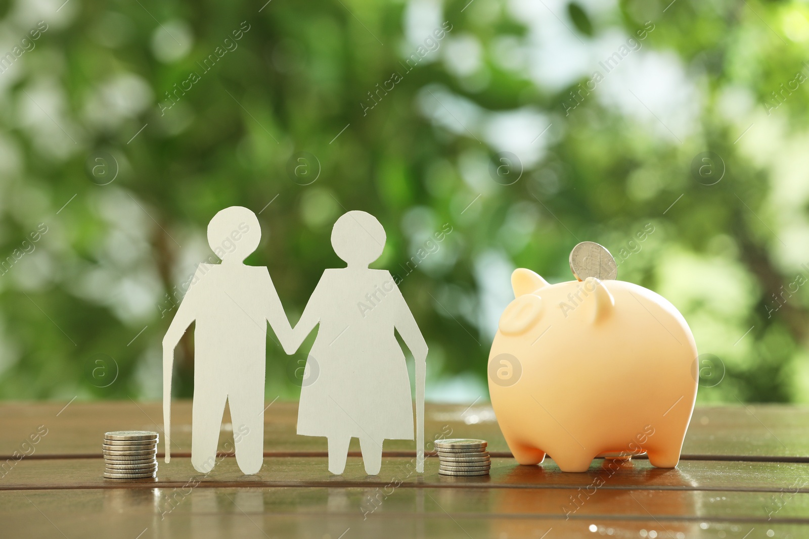 Photo of Pension savings. Figure of senior couple, piggy bank and stacked coins on wooden table outdoors