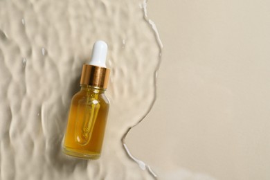 Photo of Bottle of cosmetic oil in water on beige background, top view. Space for text