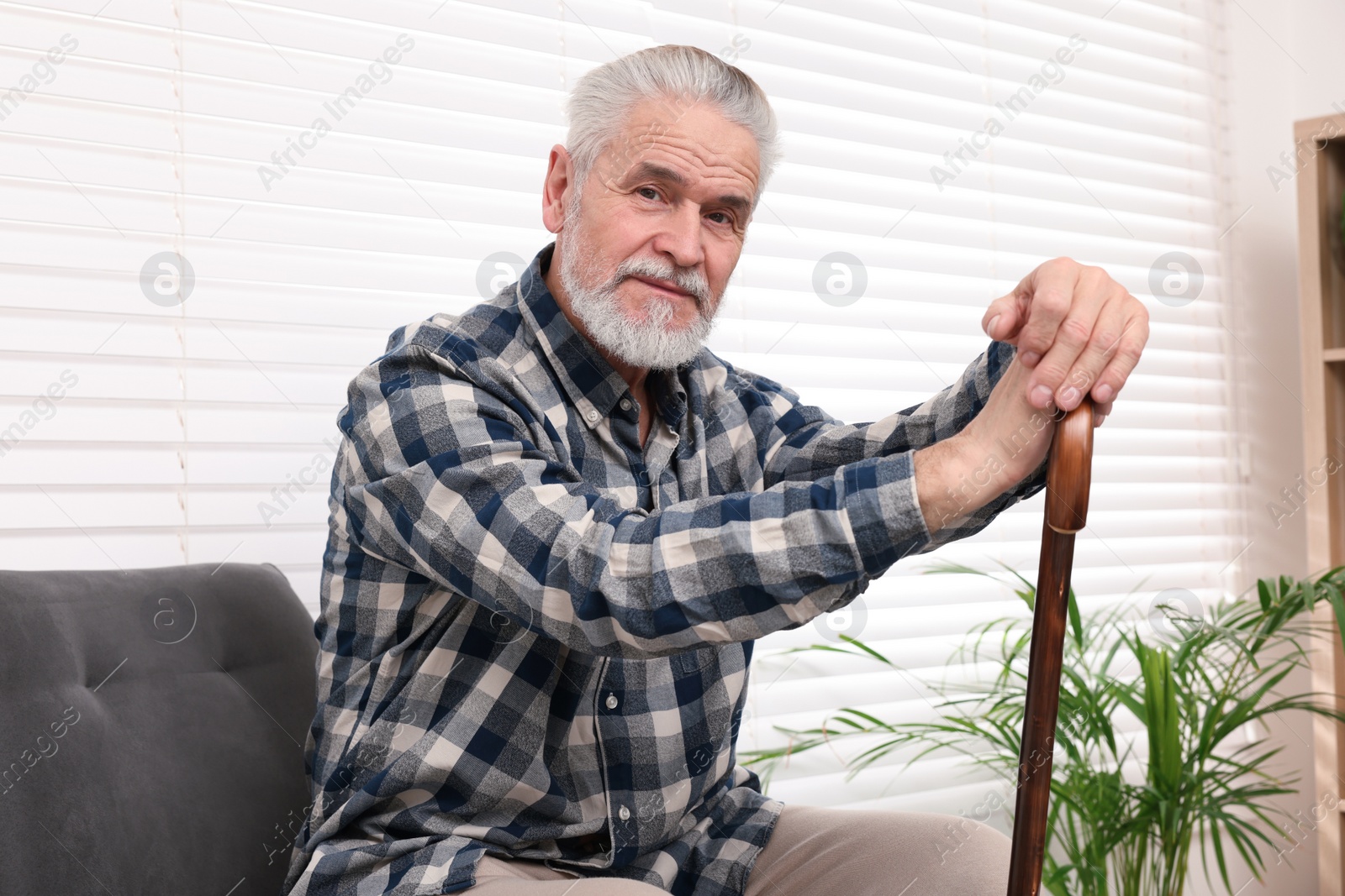 Photo of Senior man with walking cane sitting on armchair at home