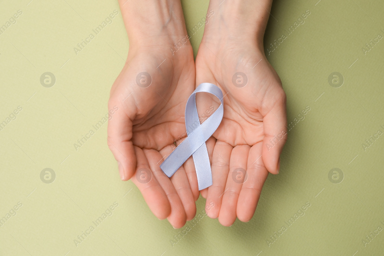 Photo of International Psoriasis Day. Woman with light blue ribbon as symbol of support on green background, top view