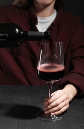 Alcohol addiction. Woman pouring red wine from bottle into glass at dark textured table, closeup