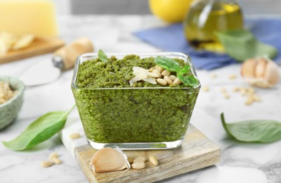 Photo of Delicious pesto sauce and ingredients on white marble table