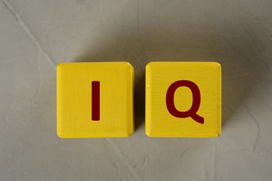 Photo of Yellow cubes with abbreviation IQ on light grey stone table, flat lay