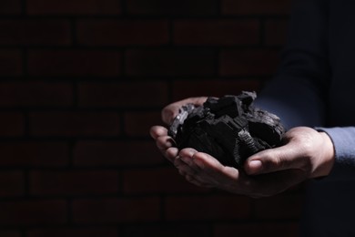 Man with handful of coal near brick wall, closeup. Space for text
