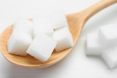 Photo of Many sugar cubes and wooden spoon on white table, closeup