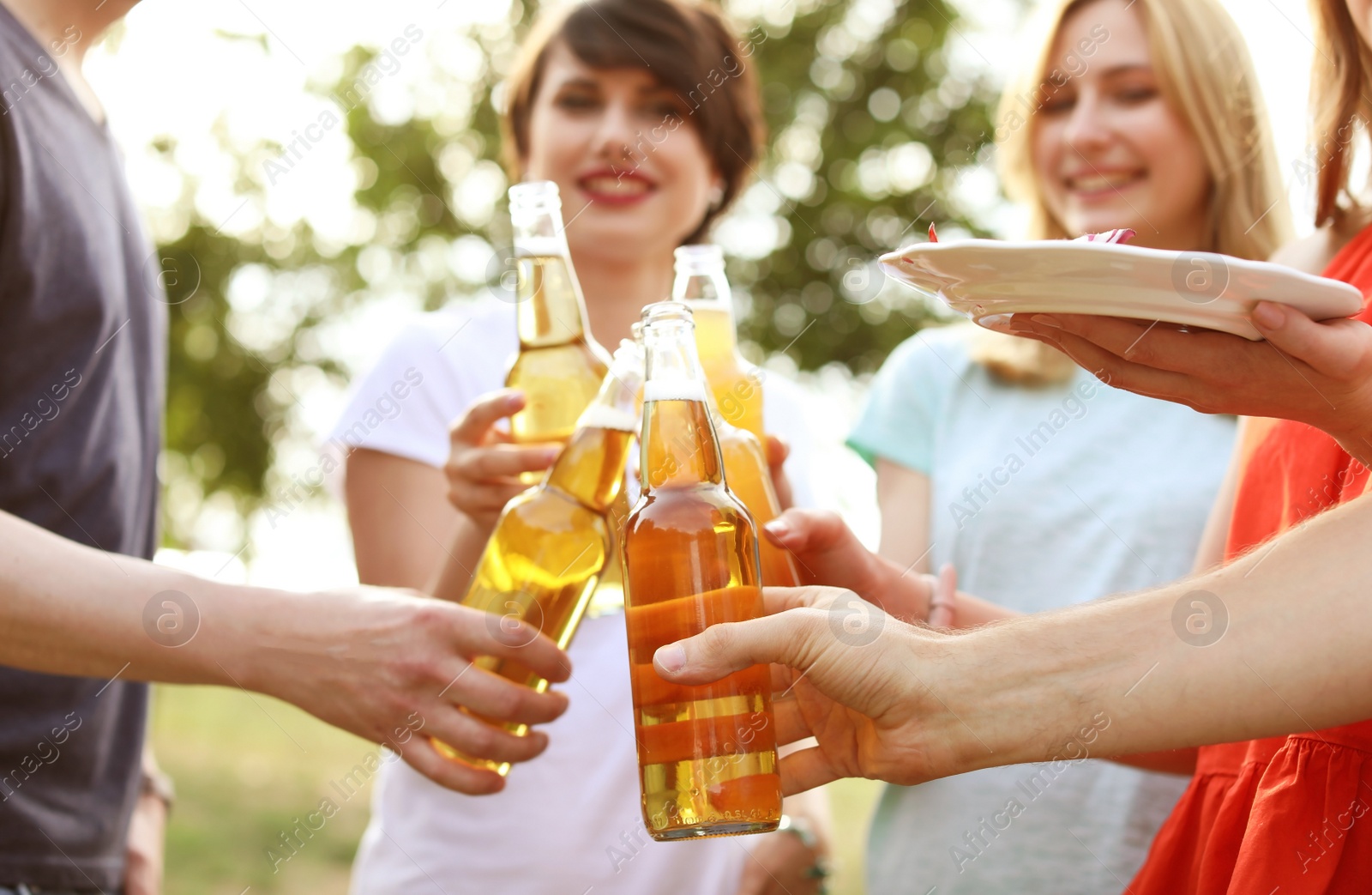 Photo of Young people with bottles of beer and food outdoors. Summer barbecue