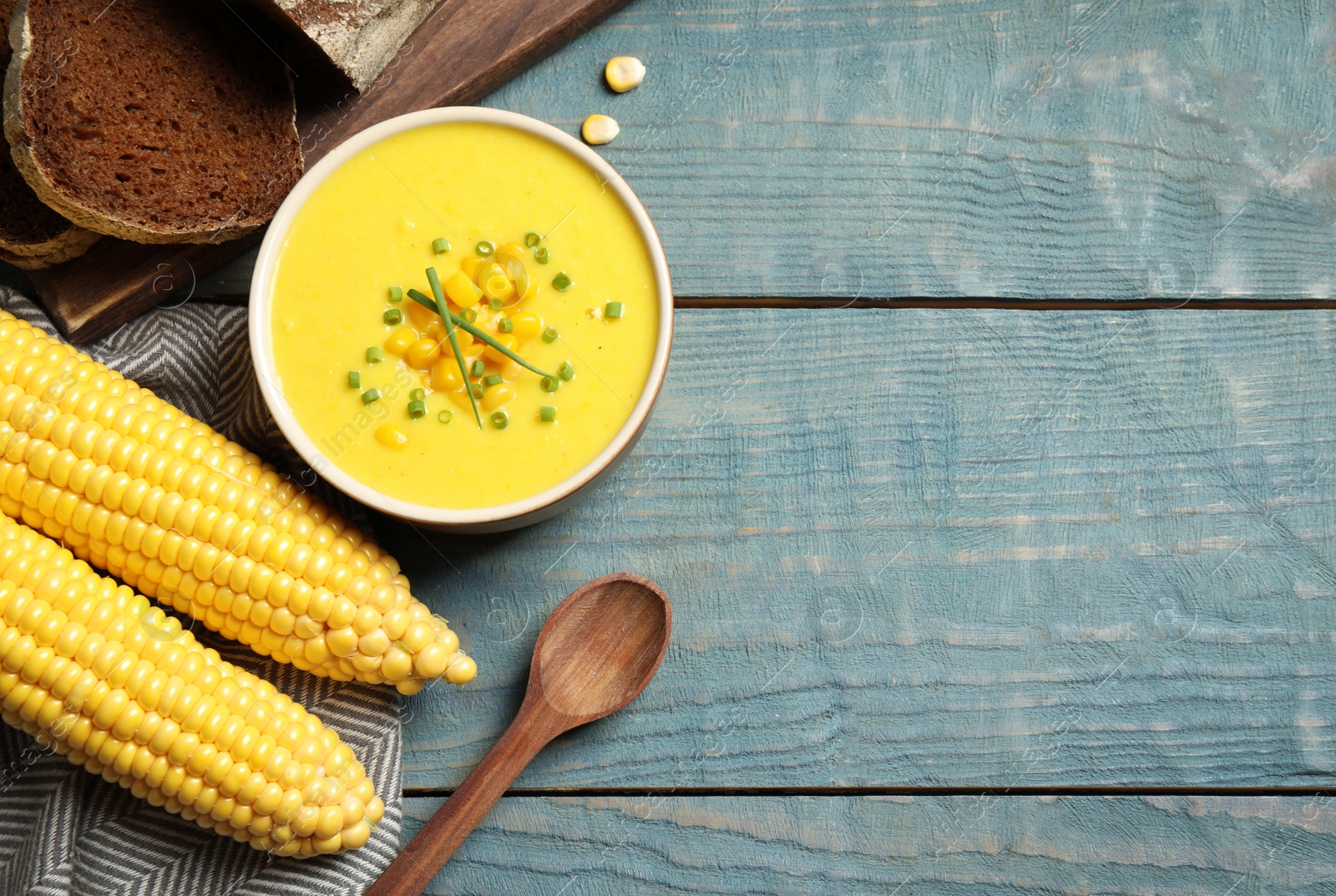 Photo of Delicious creamy corn soup served on blue wooden table, flat lay. Space for text