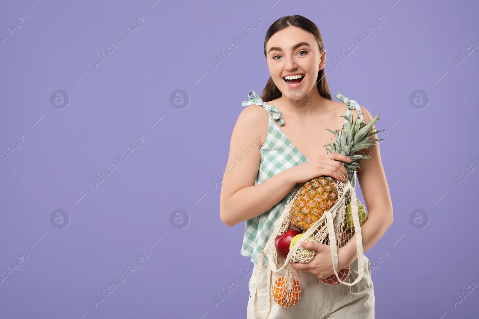 Photo of Woman with string bag of fresh fruits on violet background, space for text