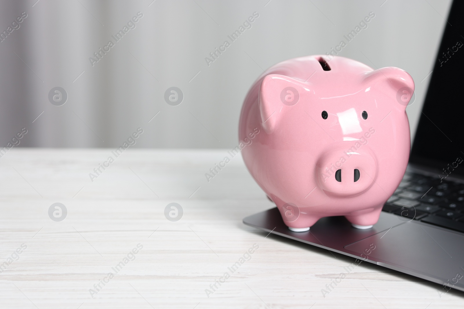 Photo of Piggy bank and laptop on white table indoors. Space for text