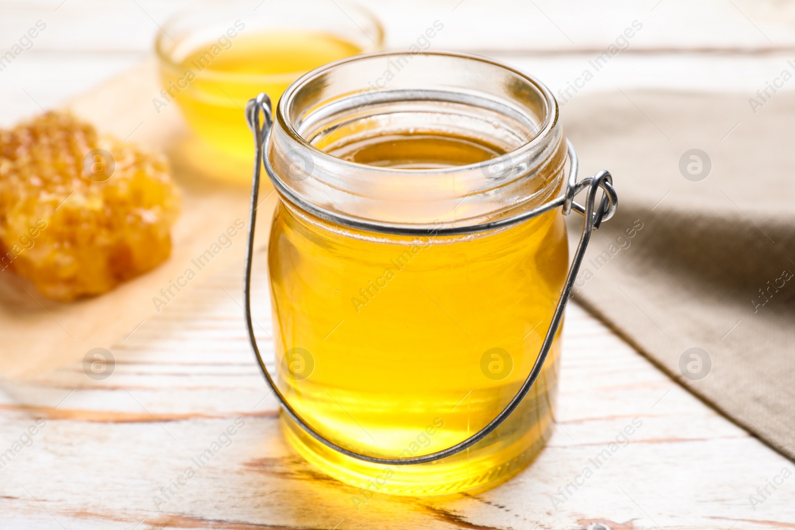 Photo of Tasty aromatic honey in glass jar on white wooden table