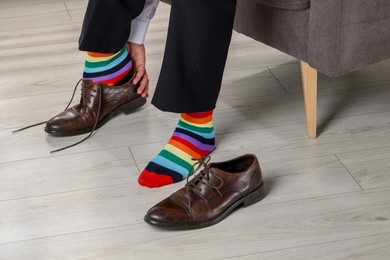 Man with colorful socks putting on stylish shoes indoors, closeup