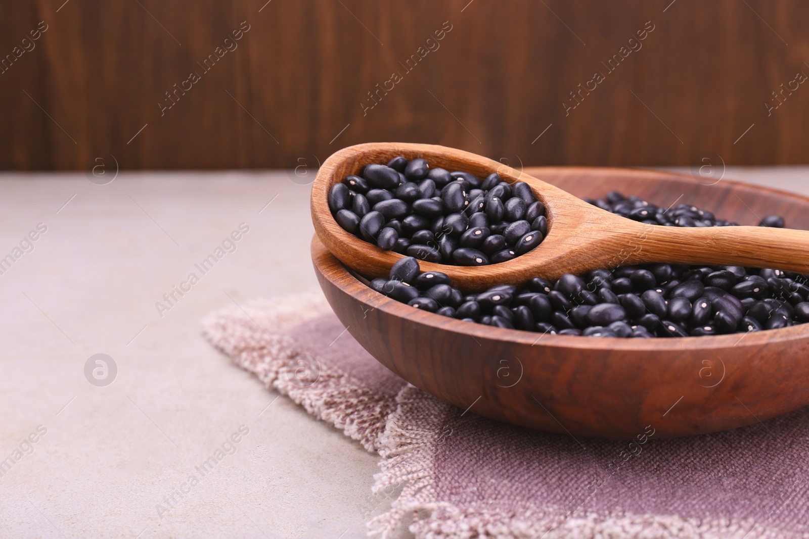 Photo of Bowl and spoon of raw black beans on light grey table, closeup. Space for text