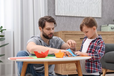 Photo of Dad and son making paper boats at coffee table indoors