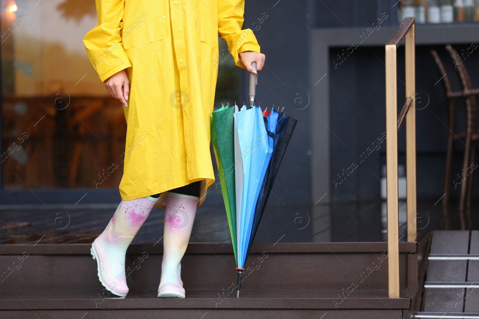 Image of Woman wearing raincoat and rubber boots holding umbrella outdoors, closeup