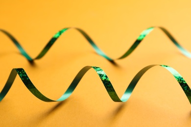 Shiny green serpentine streamers on orange background, closeup