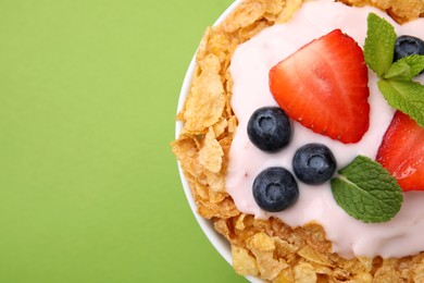 Delicious crispy cornflakes, yogurt and fresh berries in bowl on green background, top view with space for text. Healthy breakfast