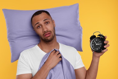 Photo of Tired man with pillow and alarm clock on orange background. Insomnia problem