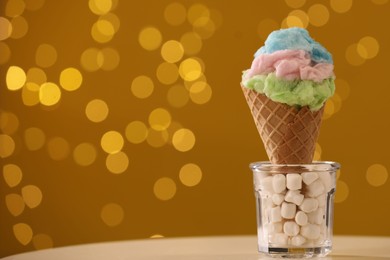 Photo of Sweet cotton candy in waffle cone on table against blurred lights, closeup. Space for text