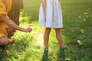 Photo of Mother applying insect repellent onto girl's leg in park, closeup