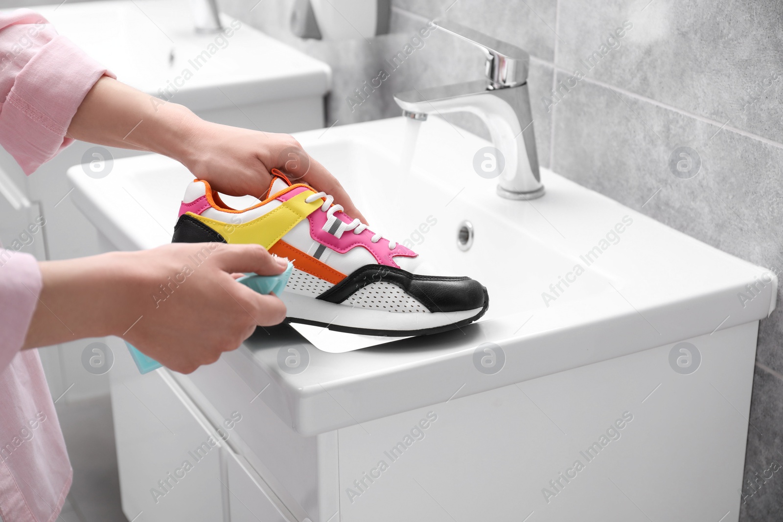 Photo of Woman washing stylish sneakers with brush in sink, closeup