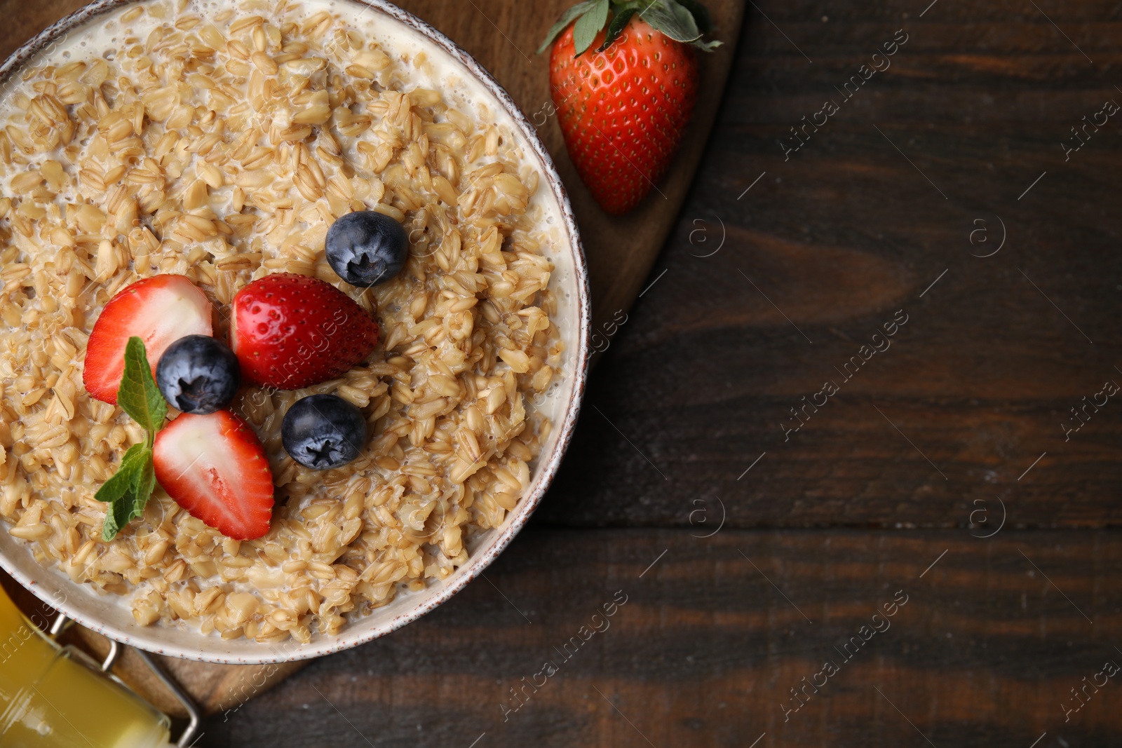 Photo of Tasty oatmeal with strawberries and blueberries in bowl on wooden table, flat lay. Space for text