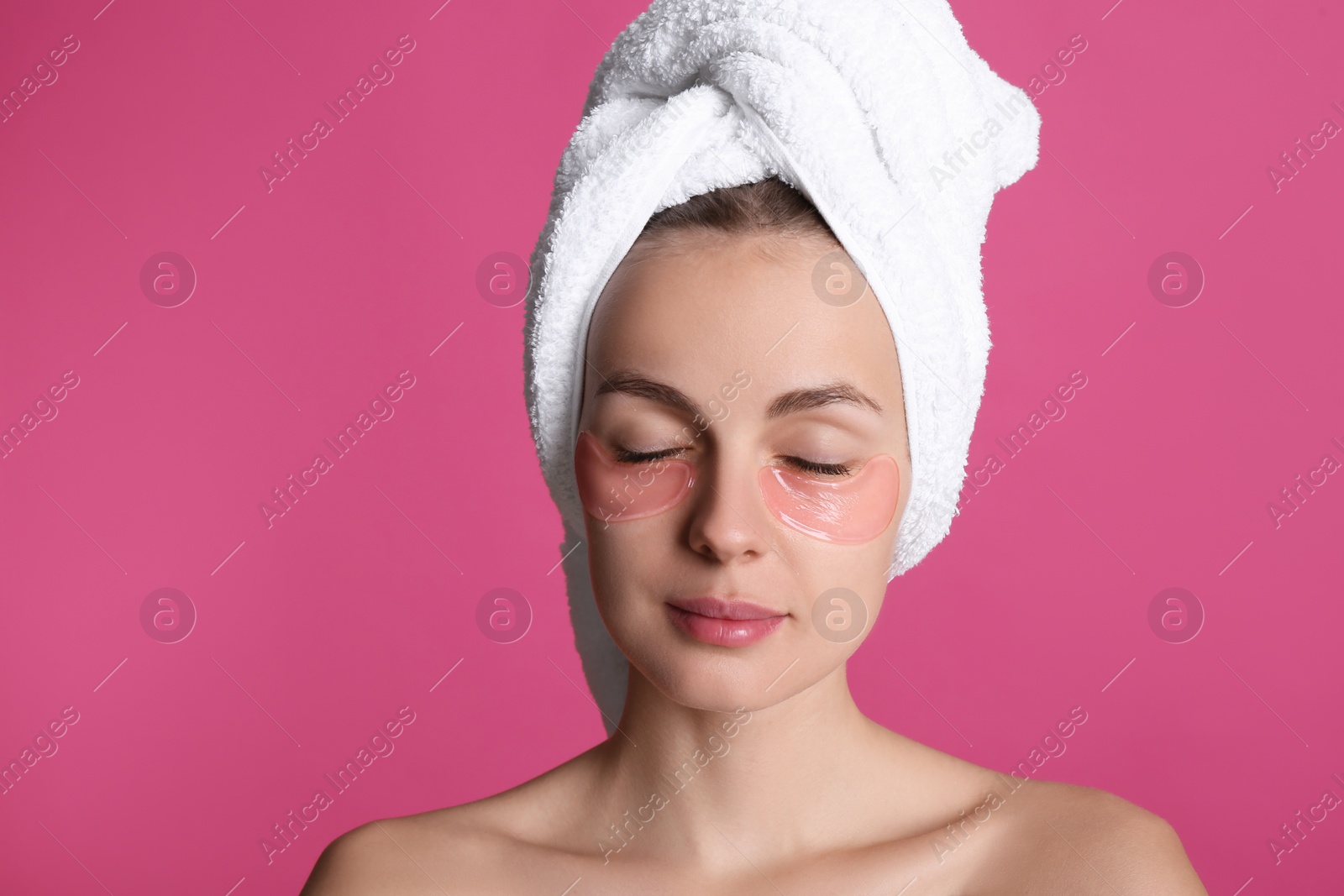 Photo of Beautiful young woman with under eye patches and hair wrapped in towel on pink background