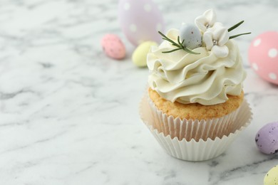 Tasty Easter cupcake with vanilla cream and candies on white marble table, space for text